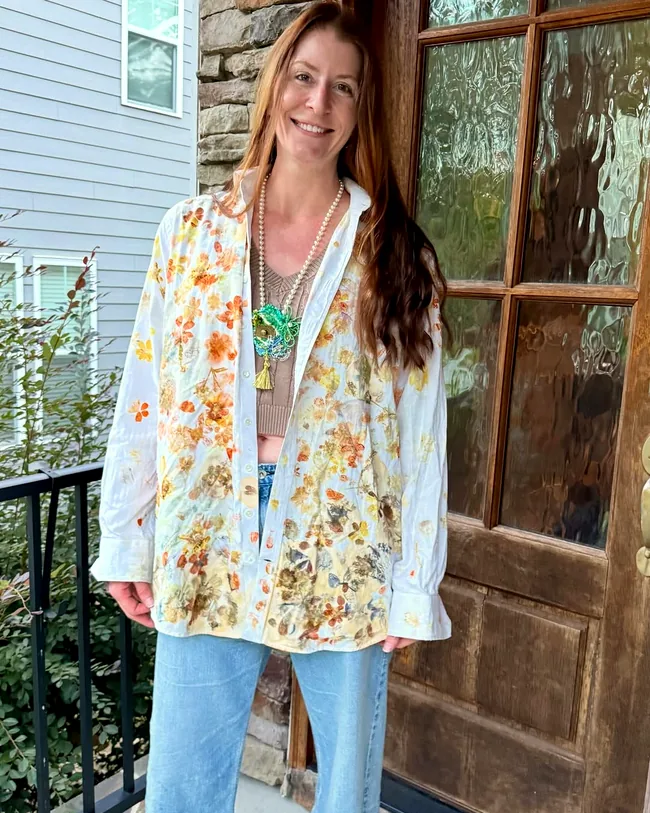 A white button-down shirt covered in pounded orange and gold flower prints, worn on a porch