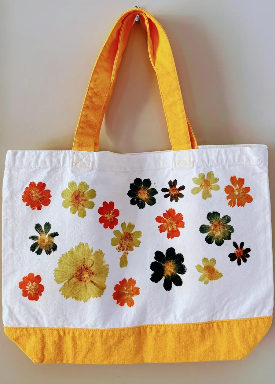 A white canvas tote covered in pressed flower prints, hanging on a wall hook