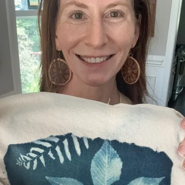 Kristi Thompson smiling and holding a canvas tote printed with a cyanotype fern
