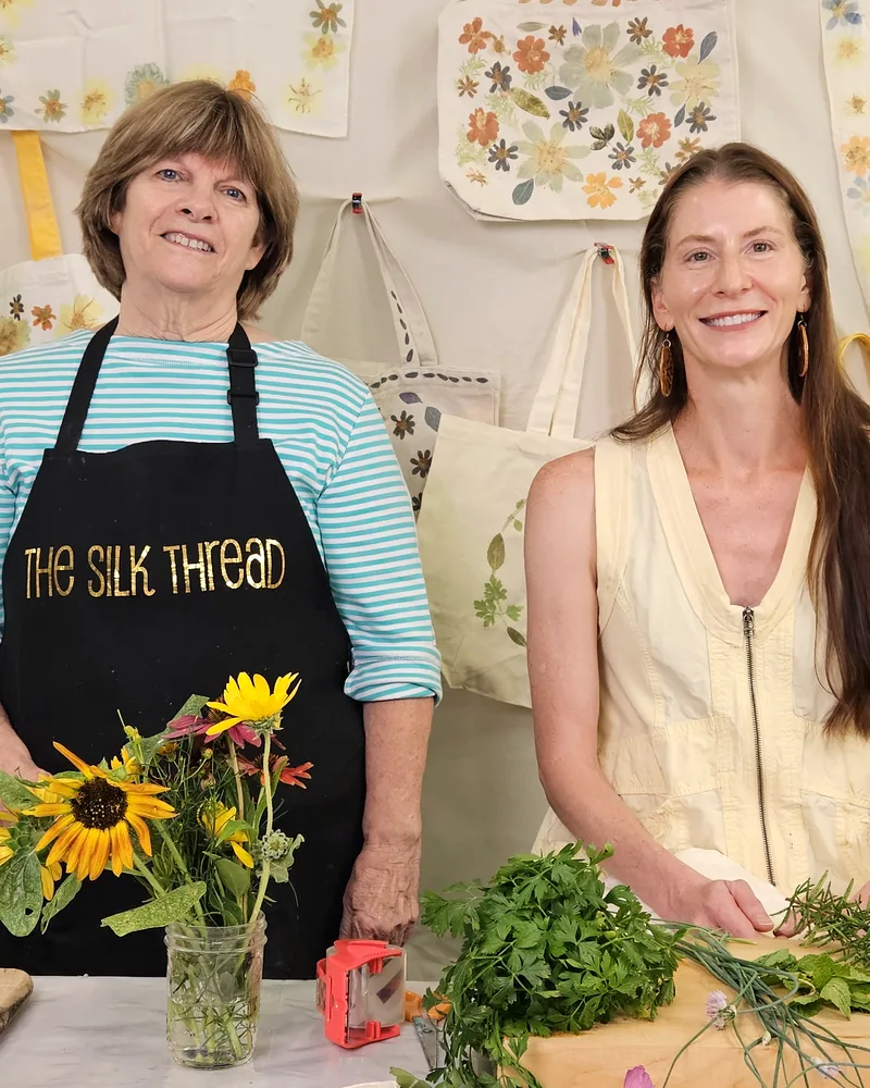 Theresa Brown and Kristi Thompson at their worktable with sunflowers and printed totes